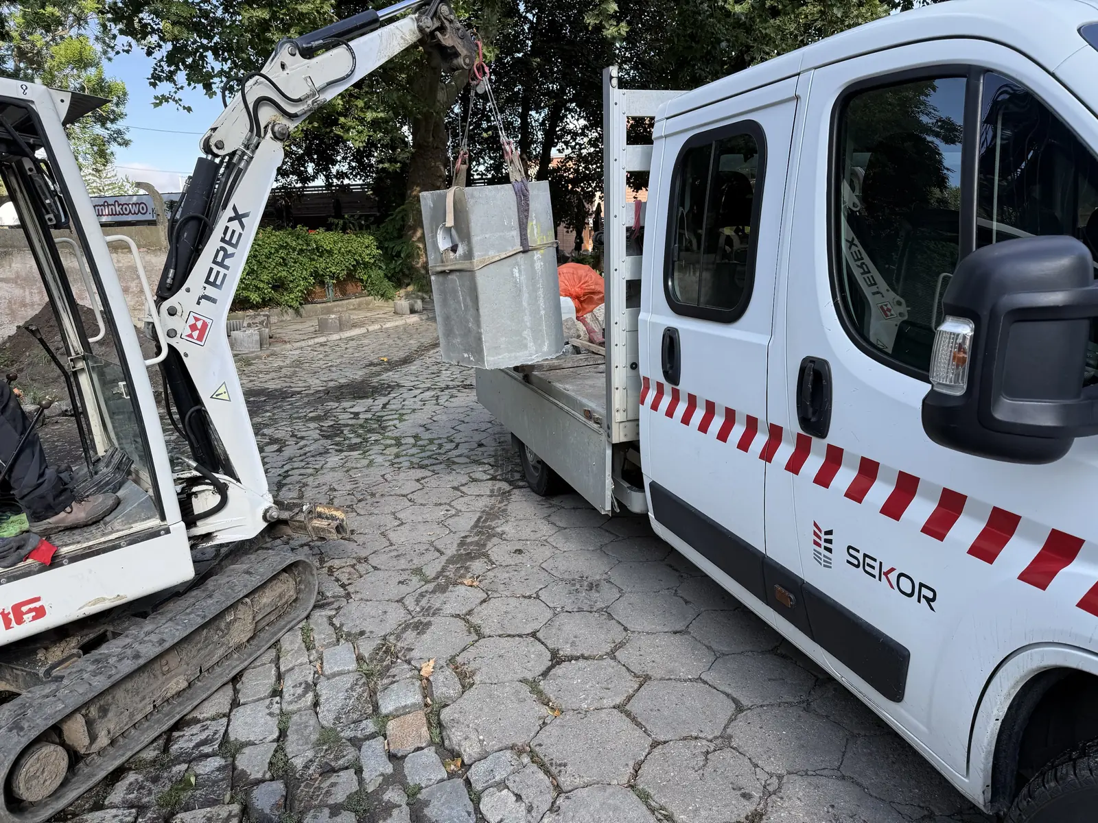 Minikoparka rozładowuje krąg betonowy z samochodu SEKOR na budowie kanalizacji we Wrocławiu