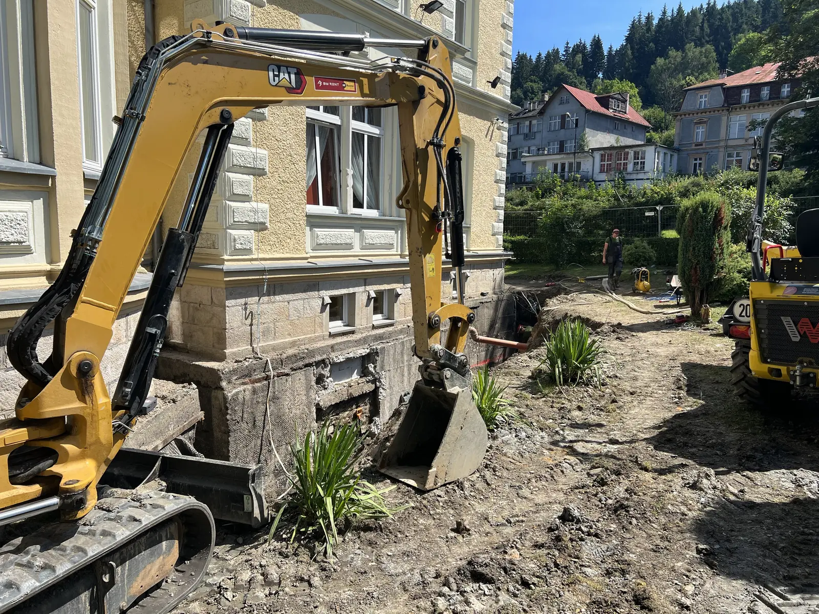 Koparka przy wykopie pod kanalizację wzdłuż zabytkowego budynku