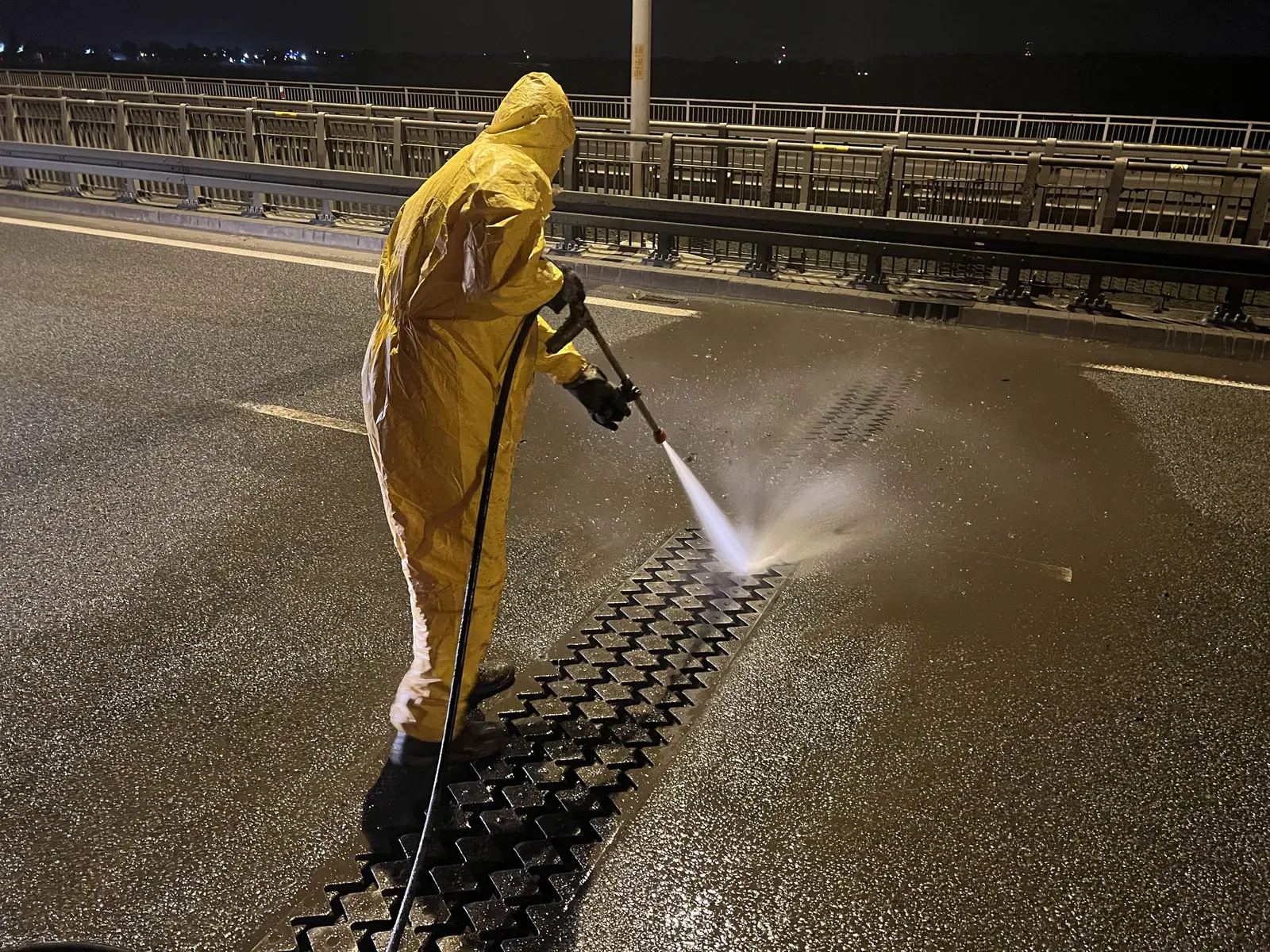 Technik SEKOR w kombinezonie czyści ciśnieniowo odwodnienie liniowe na moście nocą