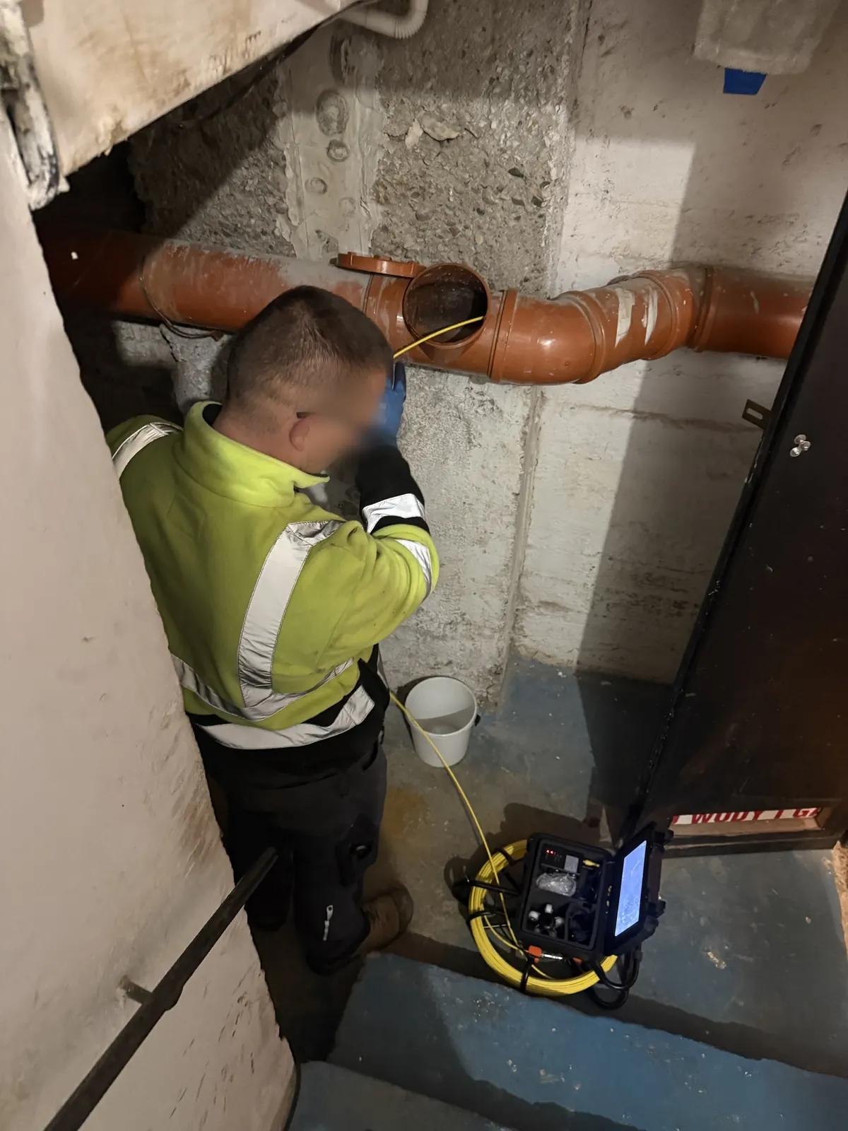 Technik SEKOR wprowadza kamerę inspekcyjną przez rewizję na instalacji kanalizacyjnej w piwnicy budynku firmy na Tarnogaju we Wrocławiu