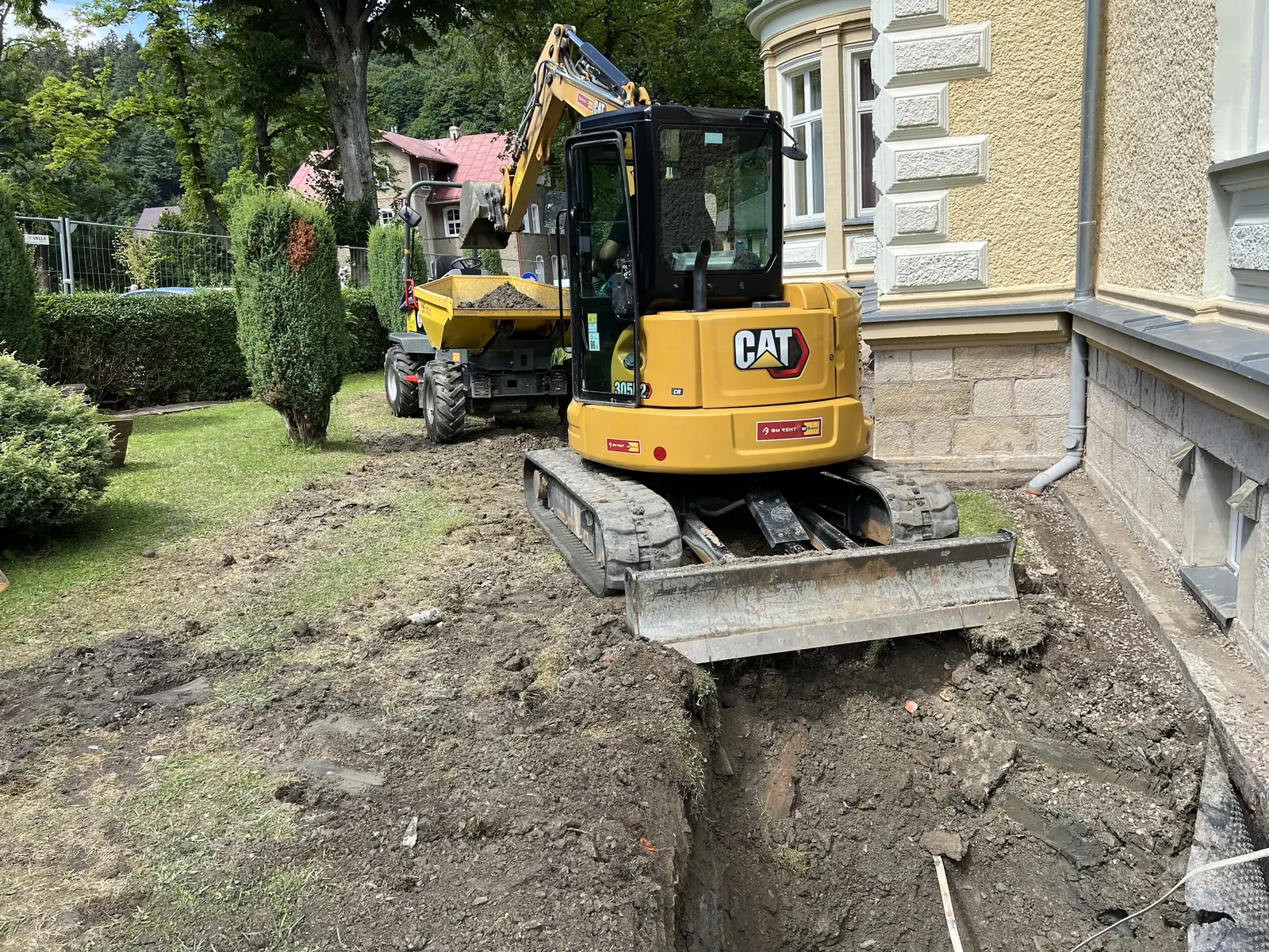 Koparka przy wykopie wzdłuż budynku, odsłonięte instalacje